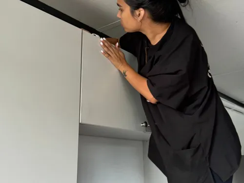 Ire Cleaning Services team member reaching to wipe the top of kitchen cabinets
