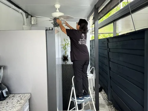 Ire Cleaning Services team member on a step ladder wiping down an outdoor ceiling fan blade