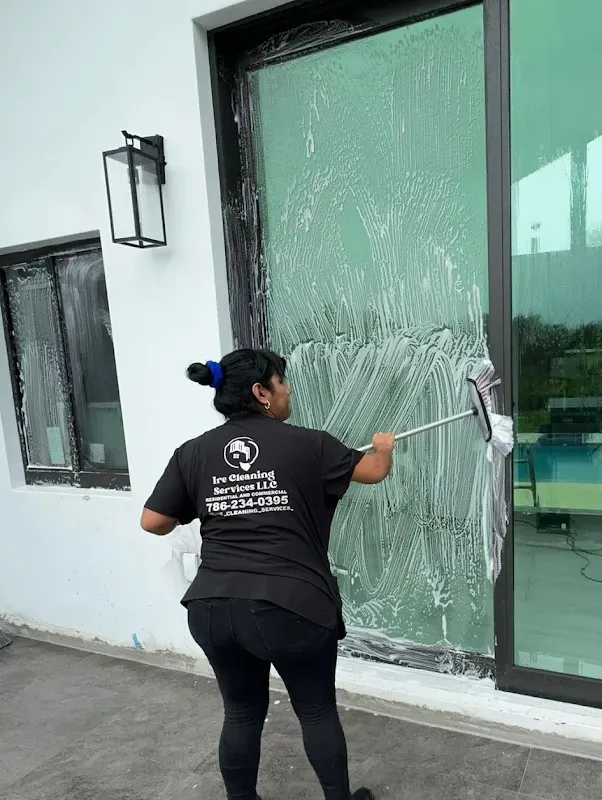 Ire Cleaning Services team member cleaning a glass sliding door on a pool patio